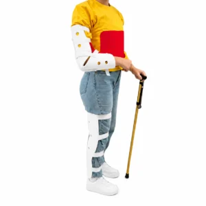 Person wearing a yellow top with a red panel, using white leg braces, a white arm brace, and a gold crutch on a white background to support walking.