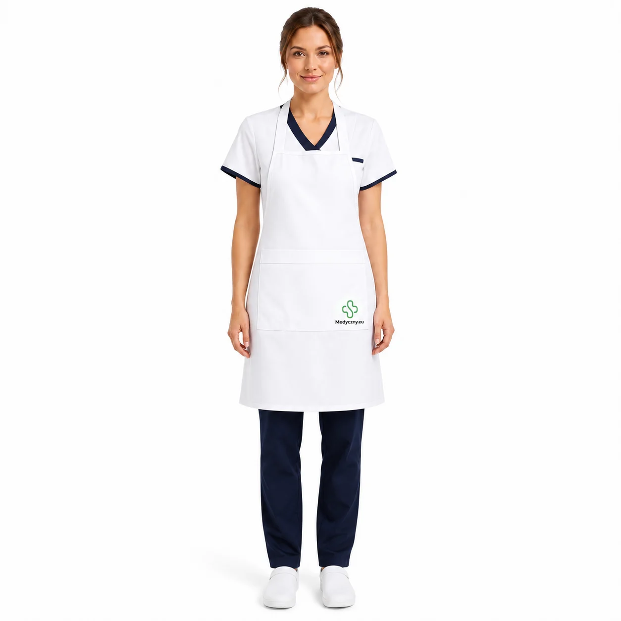 Female healthcare worker wearing a white apron over navy scrubs, standing and smiling at the camera.